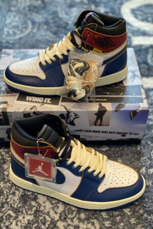 Front view of Union LA x Air Jordan 1 Storm Blue sneakers with cream laces on a themed box.
