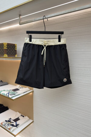 Men's black swim shorts with a contrasting cream waistband hanging on a retail display rack.