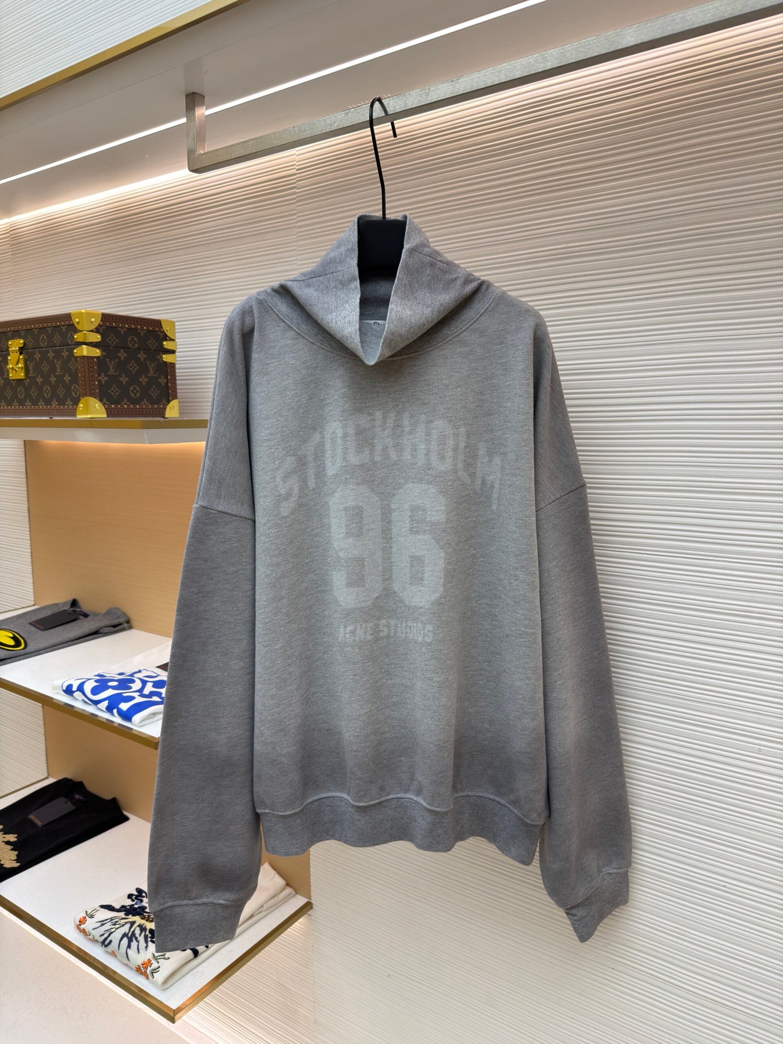 A heather grey Acne Studios oversized hoodie with a white Stockholm 96 chest graphic hanging in a boutique.