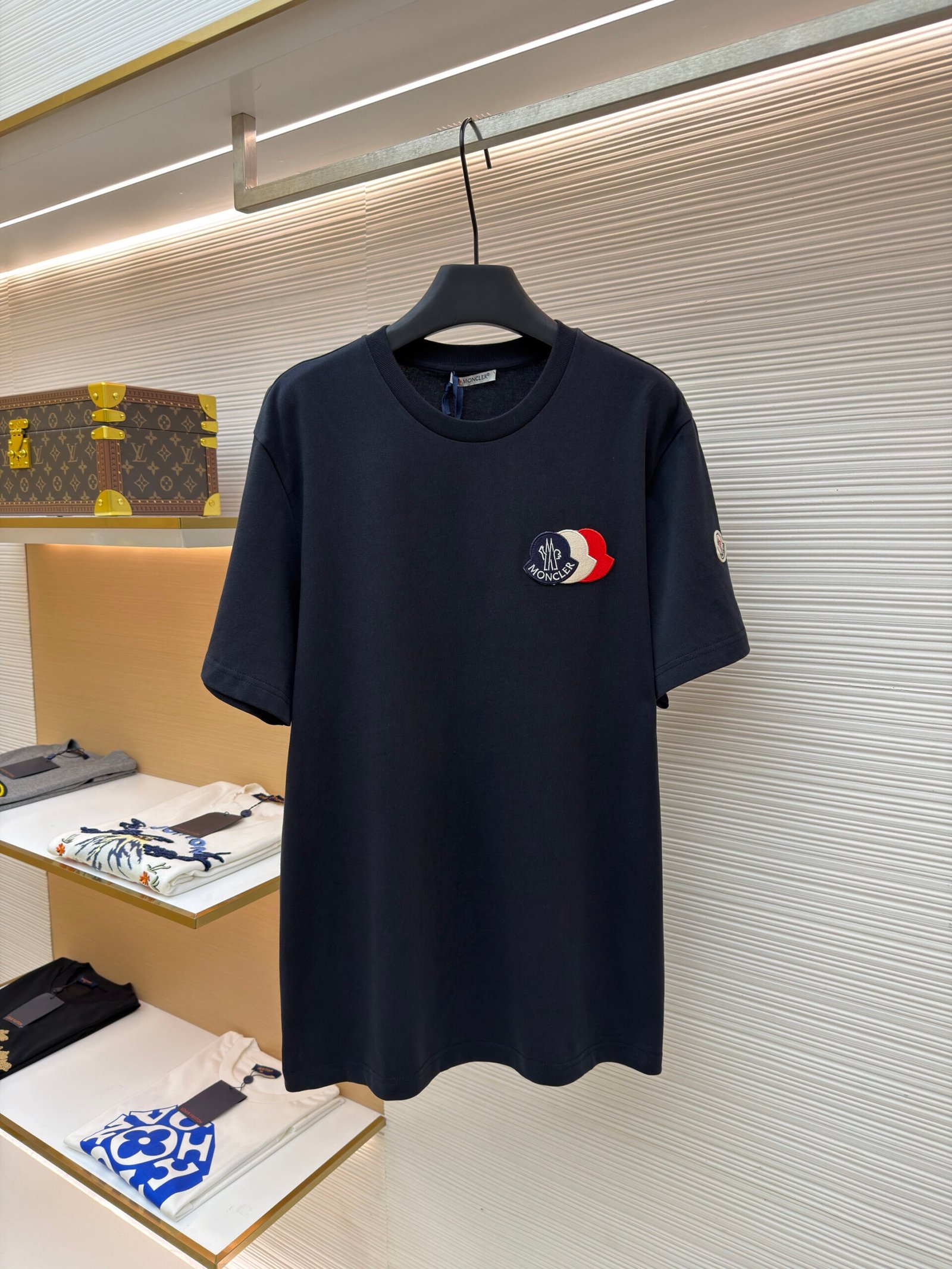 A deep navy blue men's cotton T-shirt featuring a unique triple-layered designer logo patch hanging on a display rack.