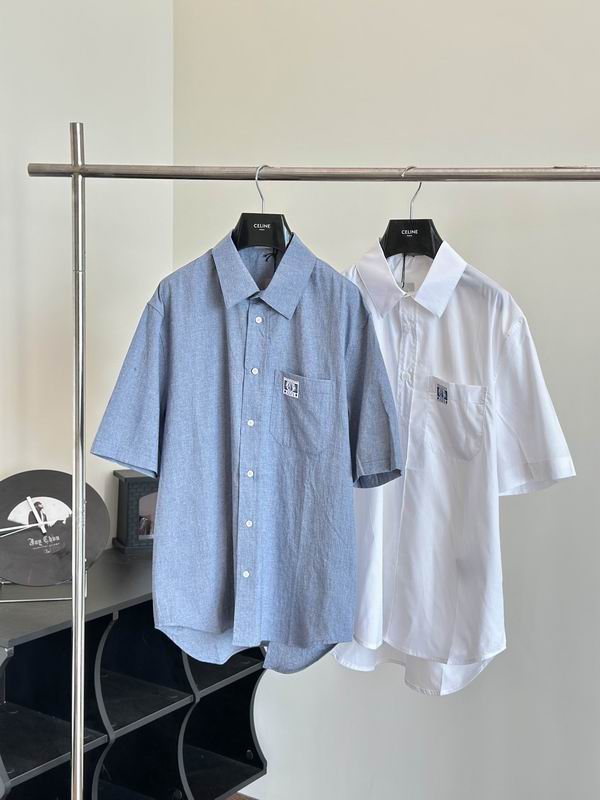 Two men’s short-sleeve button-down shirts hanging on a silver rack. One is a textured chambray blue and the other is a crisp white, both featuring a square patch logo on the front chest pocket.