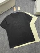 A stack of three premium men's t-shirts in black, charcoal grey, and pale yellow, featuring a large tonal embossed Miu Miu logo on the center chest.