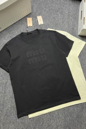 A stack of three premium men's t-shirts in black, charcoal grey, and pale yellow, featuring a large tonal embossed Miu Miu logo on the center chest.