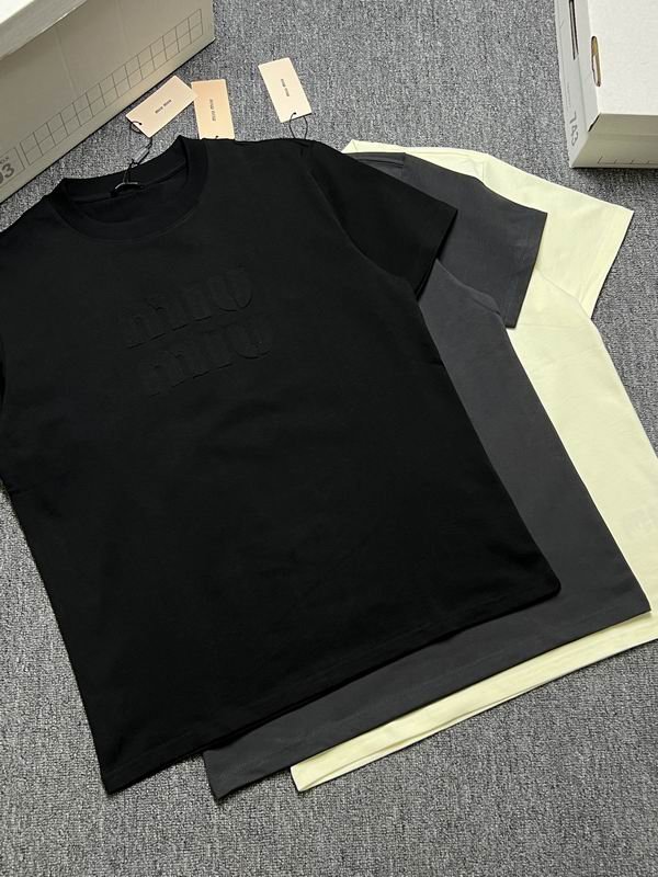 A stack of three premium men's t-shirts in black, charcoal grey, and pale yellow, featuring a large tonal embossed Miu Miu logo on the center chest.
