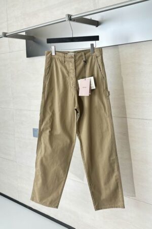 A pair of khaki-colored men's chino trousers hanging on a silver garment rack, featuring front slant pockets, reinforced stitching, and a classic button closure with original tags attached.