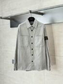 A premium men's light grey and white vertically striped corduroy overshirt hanging on a rack, featuring black buttons and the Stone Island compass badge on the left sleeve.