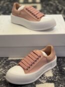 Side view of pink Alexander McQueen Deck canvas sneakers with white rubber soles on a white box.