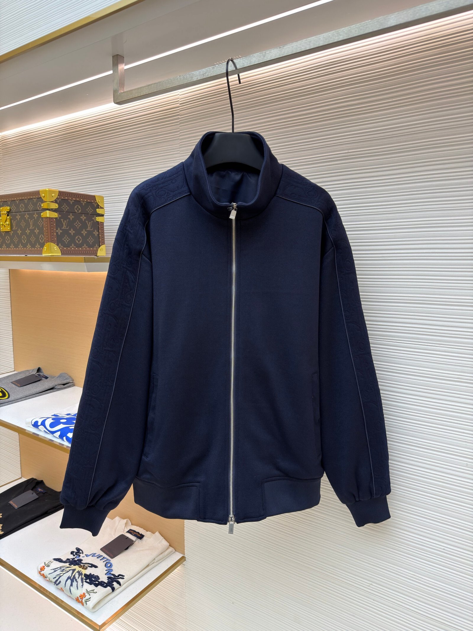 A navy blue zip-up track jacket featuring tonal Dior Oblique monogram patterns on the shoulders and sleeves.