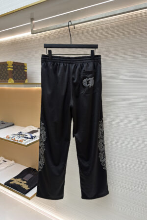 Black mesh track pants with white floral vine graphics on the sides and a Gothic CH logo on the back pocket, hanging on a display rack.