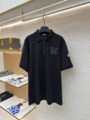 A navy blue men's pique polo shirt featuring a cream-outlined varsity "M" on the chest and a designer sleeve patch hanging on a rack.