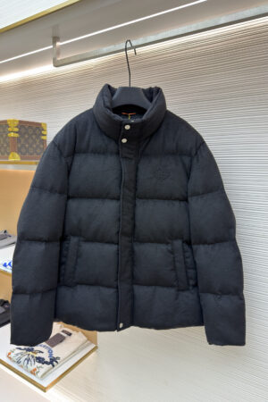 Black wool-textured puffer jacket with a tonal embroidered crest on the chest hanging on a retail display rack.