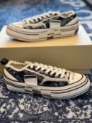 A pair of Maison Mihara Yasuhiro Peterson sneakers featuring a black and white bandana paisley print, chunky warped white midsoles, and frayed edges, resting on a blue patterned rug.