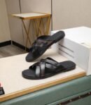 Side view of Berluti Scritto Venezia leather multi-strap sandals in a nero grigio patina with black contoured soles, displayed on a beige surface next to a white box.