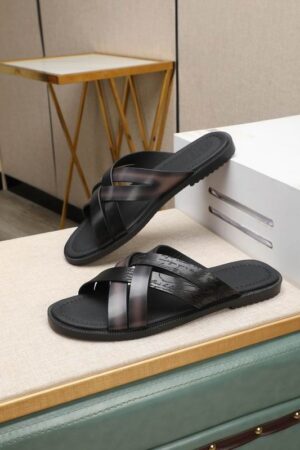 Side view of Berluti Scritto Venezia leather multi-strap sandals in a nero grigio patina with black contoured soles, displayed on a beige surface next to a white box.
