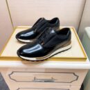 Top-down view of polished black Berluti Fast Track sneakers with Scritto engravings and a layered white and tan midsole on a white box.