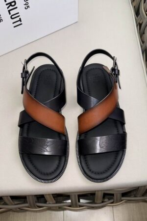 Top-down view of Berluti Cross sandals featuring a radiant tobacco brown patina leather strap, black Scritto engraved straps, and a thick black comfort sole.