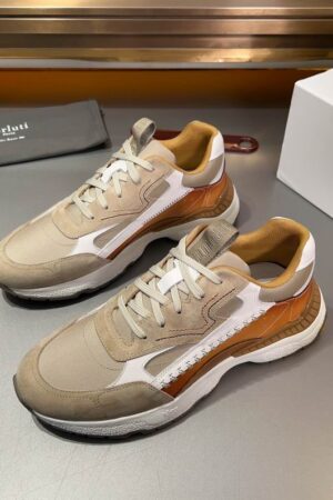 Angled view of Berluti Sky Running sneakers featuring beige suede, mesh panels, tobacco leather accents, and thick white soles on a grey surface.