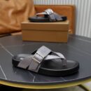 Pair of grey Berluti Scritto leather thong sandals with silver buckles and black contoured soles displayed on a brown box and black table.