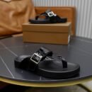Top-down view of black patent leather Berluti Scritto thong sandals with silver buckles and contoured soles displayed on a grey table.