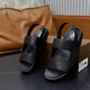Top-down view of black Berluti Lorenzo leather sandals featuring iconic Scritto engravings and ergonomic black footbeds on a dark marble table.