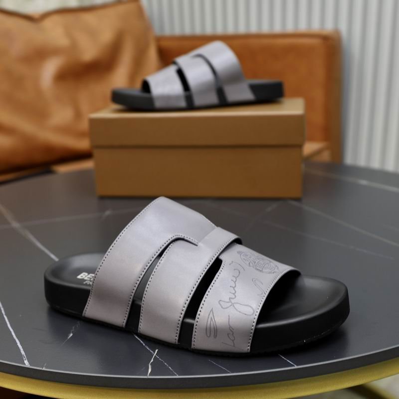 Pair of grey Berluti Scritto leather sandals with a unique H-strap design and black contoured soles displayed on a black table with a brown box.