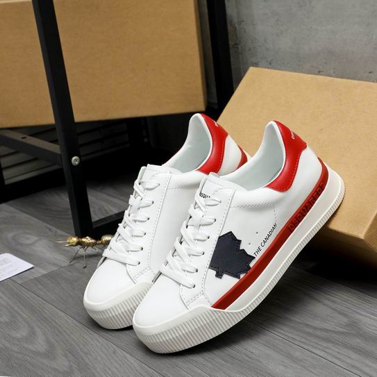 A pair of DSQUARED2 The Canadian low-top sneakers in white leather, featuring a red heel tab, a red side stripe, and a navy blue maple leaf patch, leaning against a cardboard box.