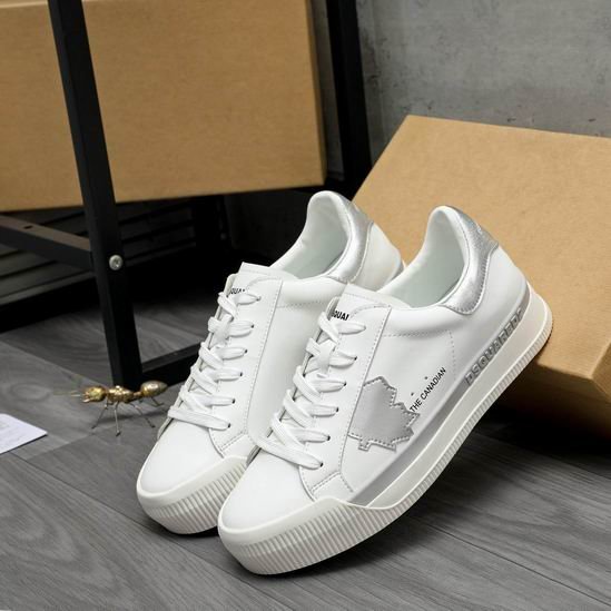 A pair of DSQUARED2 The Canadian low-top sneakers in white leather, featuring a metallic silver heel tab, a silver side stripe, and a silver maple leaf patch, leaning against a cardboard box.