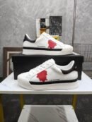 A pair of white leather Dsquared2 low-top sneakers with a red maple leaf patch on the side and a black heel tab, displayed on a marble surface.