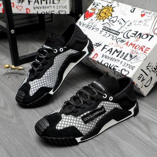 A pair of DOLCE & GABBANA NS1 low-top sneakers featuring a white honeycomb mesh upper, black suede overlays, a branded side insert, and a rugged black sole, leaning against a graffiti-printed box.