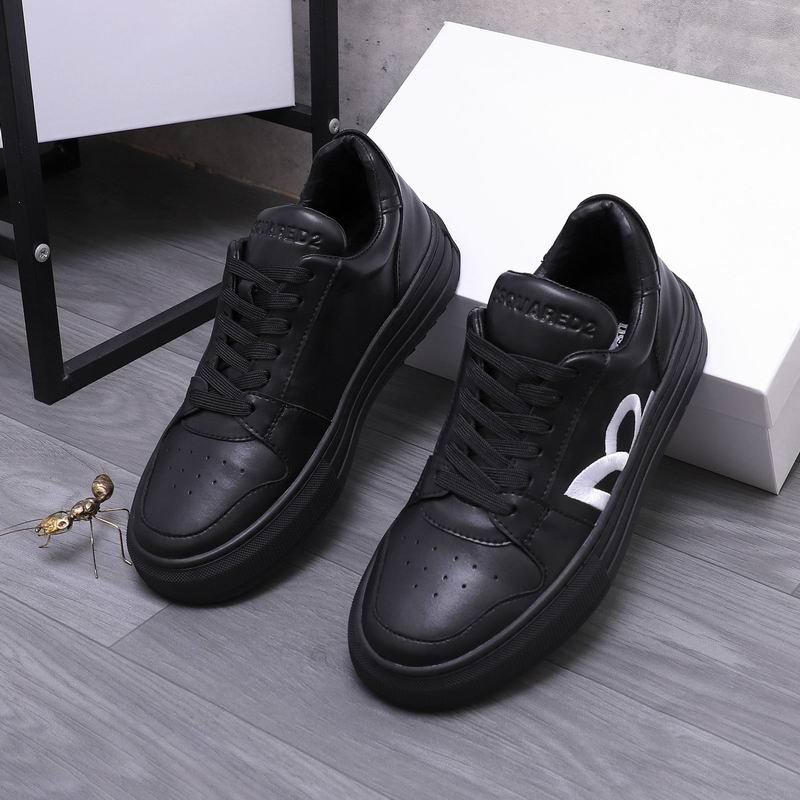 A pair of all-black leather Dsquared2 low-top sneakers with a white maple leaf graphic on the side, displayed on a gray wood surface next to a white box.