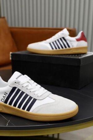 A top-down view of a pair of DSQUARED2 Boxer low-top sneakers in white leather with light gray suede toe caps, navy blue side stripes, and a bright red heel tab, displayed on a round table.
