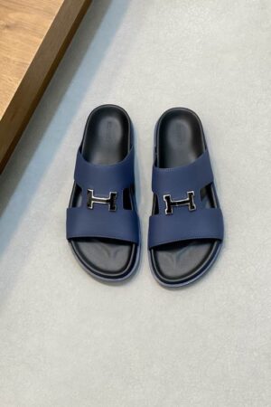Top-down view of Marine blue Hermès Chypre sandals with textured Epsom leather and silver H buckles on a grey floor.