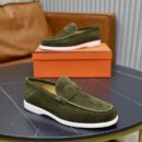 A pair of khaki green suede Hermès Sageste loafers with tonal straps and white rubber soles displayed on a black table.