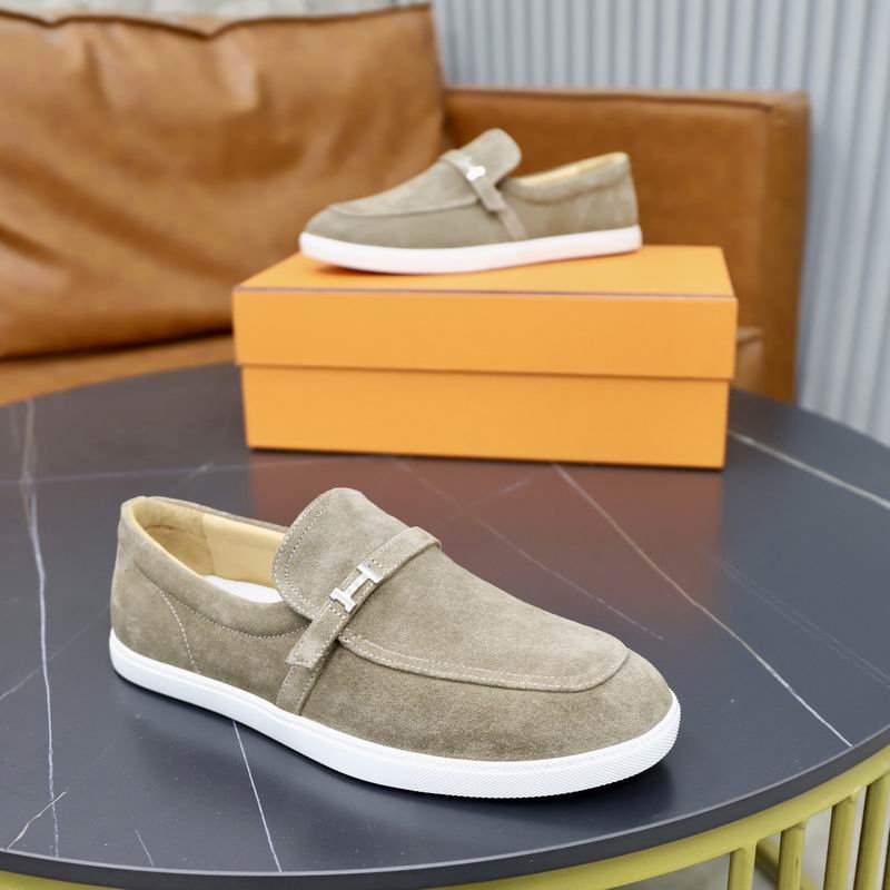 A pair of sage grey suede Hermès Mind loafers with silver H buckles and white rubber soles on a black table.