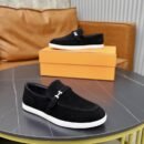 Top-down view of black Hermès Ancora loafers with silver H buckles and white soles placed on a grey marble surface.