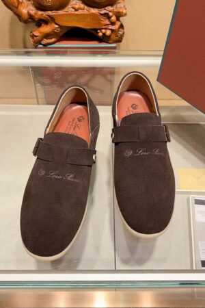 Pair of chocolate brown suede Loro Piana Summer Charms Walk loafers featuring a buckle strap closure and flexible soles displayed on a glass shelf.