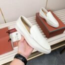 Pair of white leather Loro Piana Summer Walk loafers with matching white soles displayed on a ribbed surface with luxury packaging.