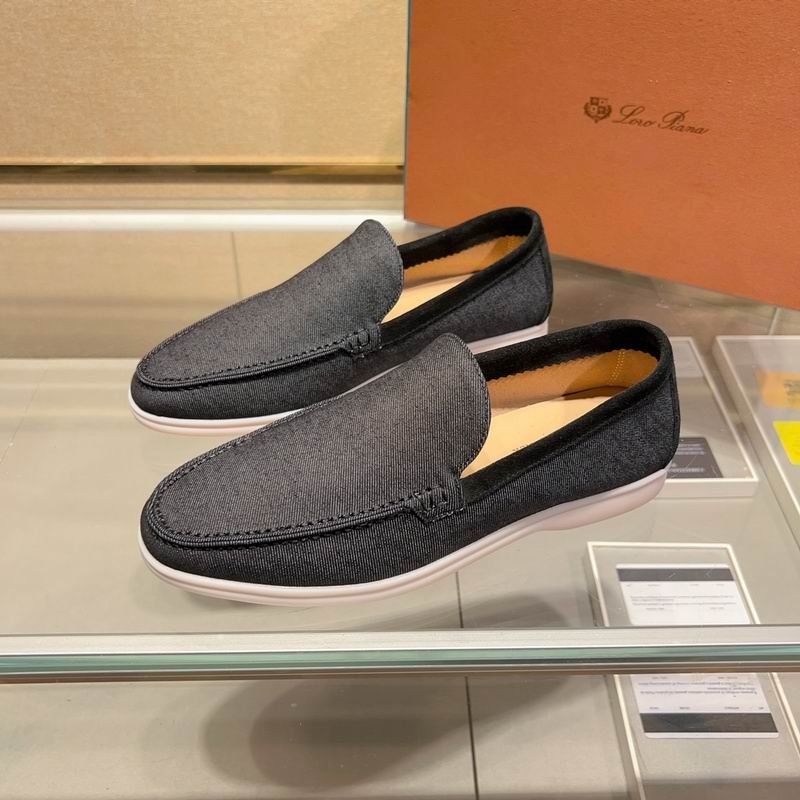 A pair of black canvas Loro Piana Summer Walk loafers with white soles displayed on a glass shelf in front of a brown designer box.