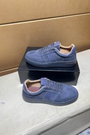 A pair of premium Loro Piana low-top sneakers in slate blue suede with tonal leather trim and a tan interior lining, resting on a black box.