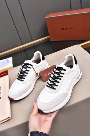 A pair of premium white Loro Piana low-top sneakers with black laces and suede trim, resting on a branded box with an attached tag.