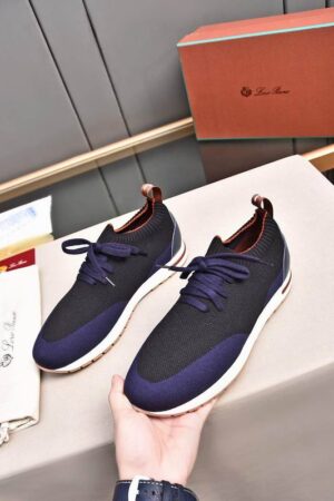 A pair of premium navy and black knitted Loro Piana low-top sneakers with a sock-like collar and white soles, displayed on a table.