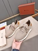 A pair of premium warm beige knitted Loro Piana low-top sneakers with a sock-like collar and a white sole, displayed on a table next to a brand box.