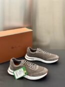 A pair of premium taupe gray Loro Piana low-top sneakers featuring technical mesh and suede paneling, displayed on a dark surface next to a brand box.
